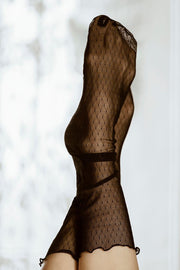 Dwie stopy w Tiulowych skarpetkach - Nocne Kropeczki unoszą się na delikatnie rozmytym, jasnym tle. Delikatna, półprzezroczysta siateczka dodaje stylizacji elegancji i zwiewności.