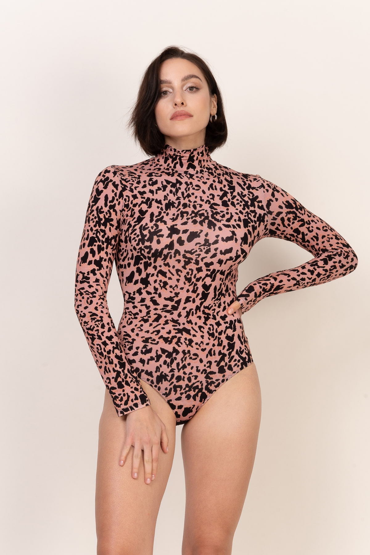 Kobieta z krótkimi ciemnymi włosami pozuje pewnie w Loungewear wiskozowe body z golfem - panterka, z jedną ręką na biodrze, a drugą przy boku, na prostym jasnym tle.