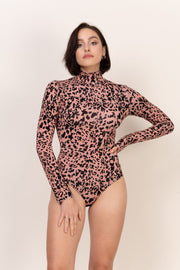 Kobieta z krótkimi ciemnymi włosami pozuje pewnie w Loungewear wiskozowe body z golfem - panterka, z jedną ręką na biodrze, a drugą przy boku, na prostym jasnym tle.