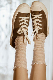Para nóg uniesionych w powietrzu, ubrana w brązowe płócienne trampki z białą podeszwą i Skarpetki kabaretki - Waniliowa Sieć - lekkie, teksturowane skarpetki idealne do stylowych stylizacji.