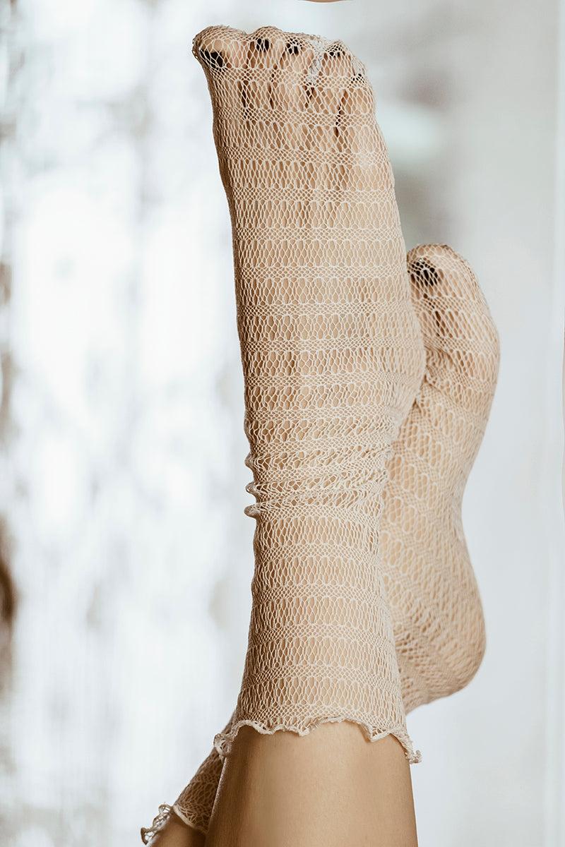 Zbliżenie dwóch stóp w kabaretkach Skarpetki - Waniliowa Sieć, z jasnobeżowym, falistym wzorem siatki idealnym do eleganckich stylizacji, na delikatnie rozmytym jasnym tle.