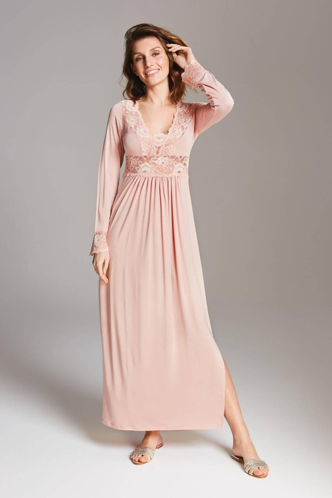 Uśmiechnięta kobieta nosi koszulkę Stars długa koszula nocna z koronką w brudny róż, z delikatną koronką przy dekolcie i mankietach. Stoi boso na prostym tle, jedną ręką dotykając włosów, a drugą trzymając u boku.